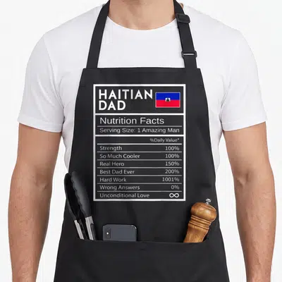 Nutrition pride apron - Nutrition label graphic listing Haitian Dad traits with flag and white blue red text — shown on a black cotton canvas apron against a white background