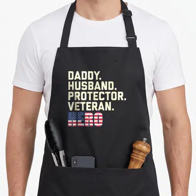 Daddy protector best husband apron - Stacked beige text reading DADDY HUSBAND PROTECTOR VETERAN above HERO filled — shown on a black cotton canvas apron against a white background