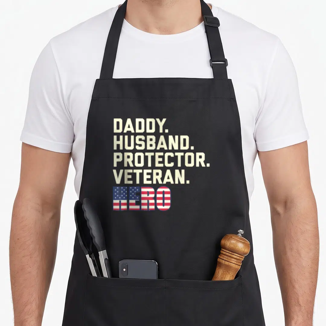 Daddy protector best husband apron - Stacked beige text reading DADDY HUSBAND PROTECTOR VETERAN above HERO filled — shown on a black cotton canvas apron against a white background