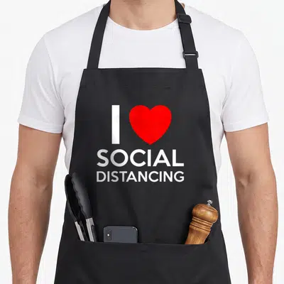 Introvert antisocial apron - I SOCIAL DISTANCING text with red heart symbol in white and red — shown on a black cotton canvas apron against a white background