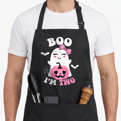 Ghost funny halloween apron - White ghost with pink bow holding pink pumpkin flanked by bats and web — shown on a black cotton canvas apron against a white background
