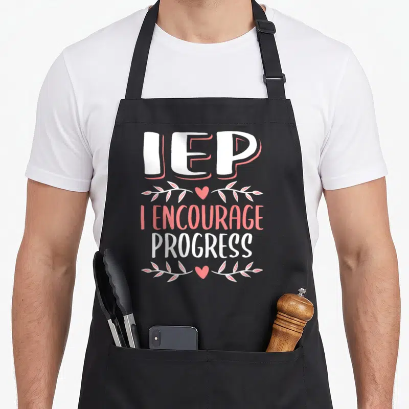 Iep encourage progress teacher apron - White and pink stacked text reading IEP I Encourage Progress with decorative — shown on a black cotton canvas apron against a white background