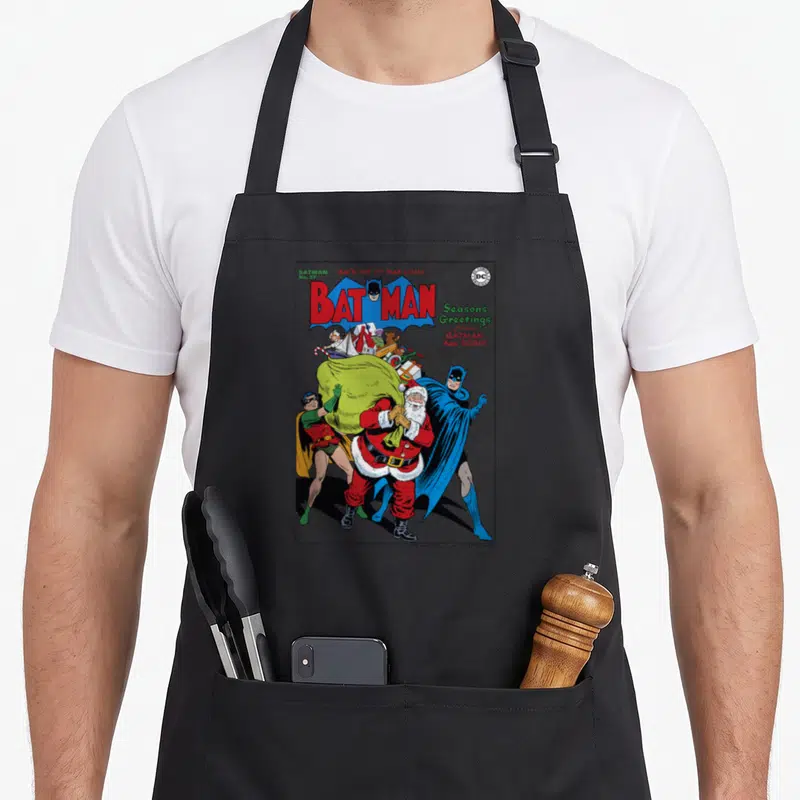Greeting christmas robin apron - Vintage Batman comic cover with Santa, War Loan text, and cartoon characters in red — shown on a black cotton canvas apron against a white background
