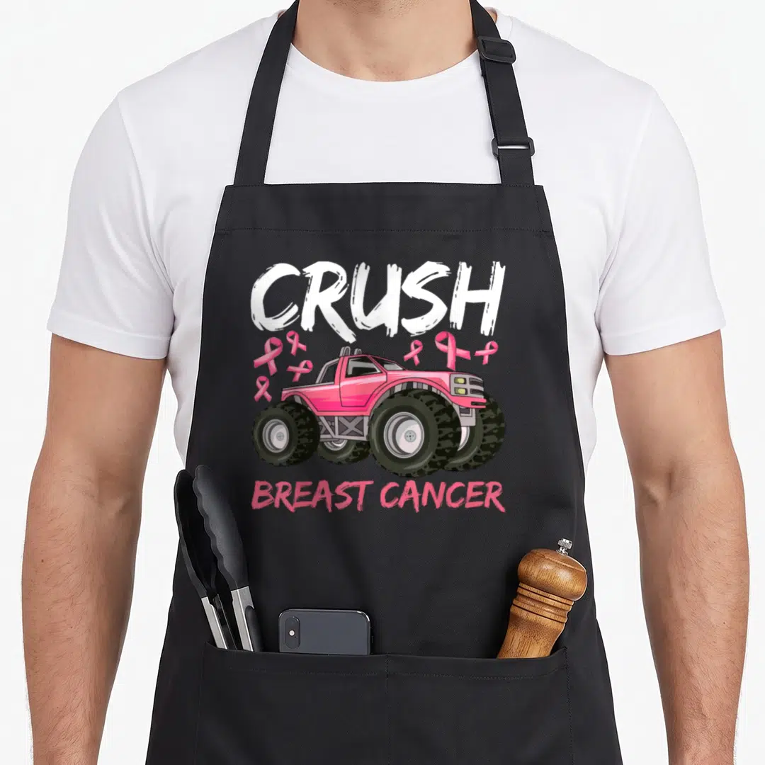 Funny toddler breast cancer awareness aprons - Pink monster truck with CRUSH BREAST CANCER text and scattered pink — shown on a black cotton canvas apron against a white background