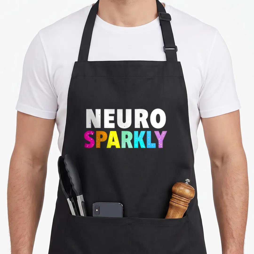 Neuro sparkly aprons - Stacked NEURO SPARKLY text in white and rainbow colors with speckled texture — shown on a black cotton canvas apron against a white background
