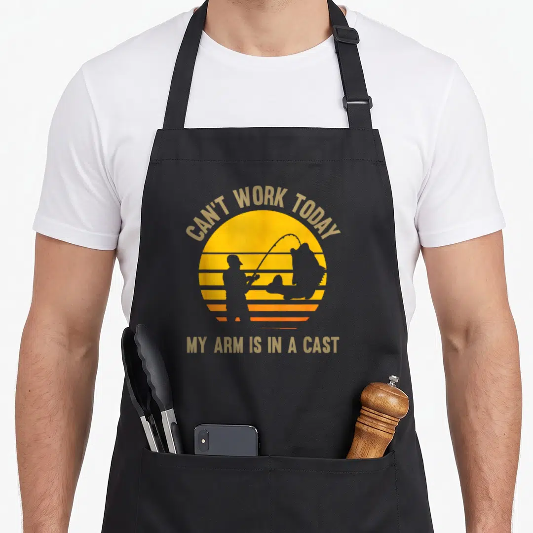 Arm fishing aprons - Yellow orange striped sun with fisherman silhouette and text Can't Work Today My Arm Is In A Cast — shown on a black cotton canvas apron against a white background