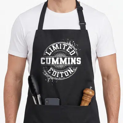 Cummin family reunion aprons - White distressed circular seal reading Limited Cummins Editon with sunburst rays — shown on a black cotton canvas apron against a white background