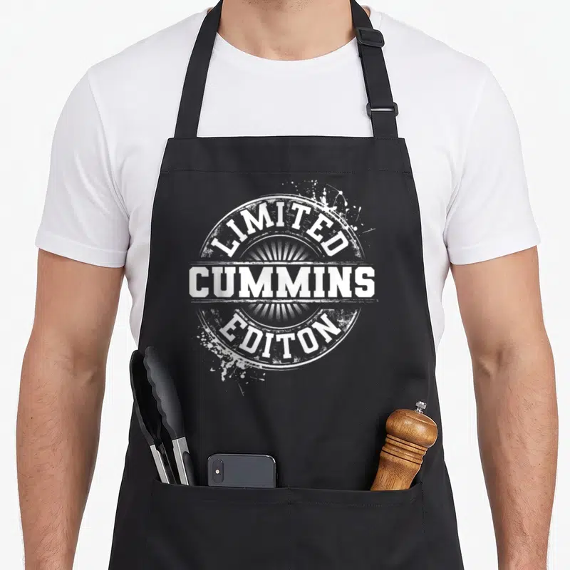 Cummin family reunion aprons - White distressed circular seal reading Limited Cummins Editon with sunburst rays — shown on a black cotton canvas apron against a white background
