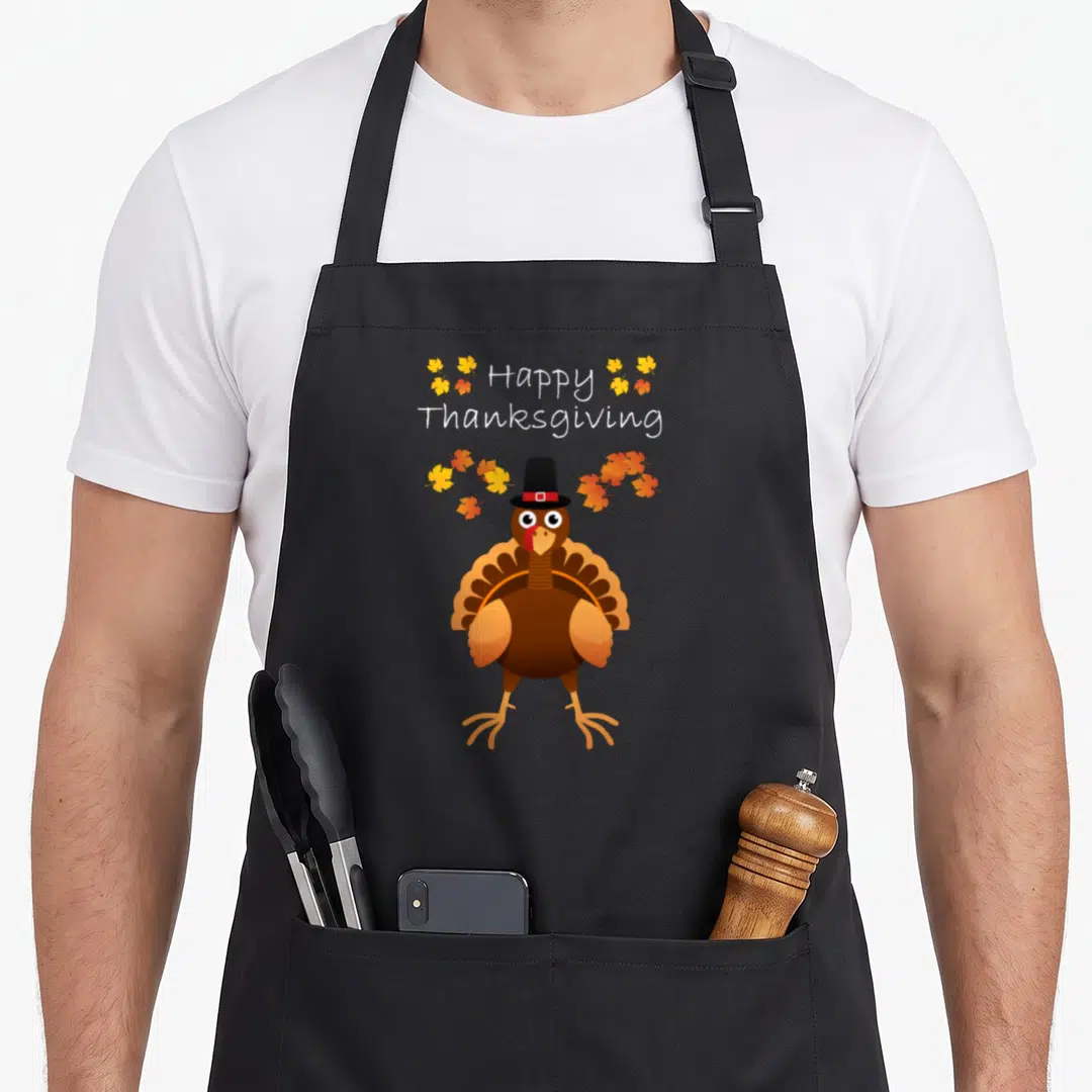 Pilgrim turkey thanksgiving day aprons - Cartoon turkey in black pilgrim hat with scattered orange and yellow leaves — shown on a black cotton canvas apron against a white background