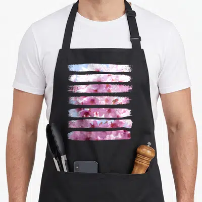 Elegant floral apron - Seven horizontal brush-stroke strips of pink and white cherry blossoms against blue sky — shown on a black cotton canvas apron against a white background