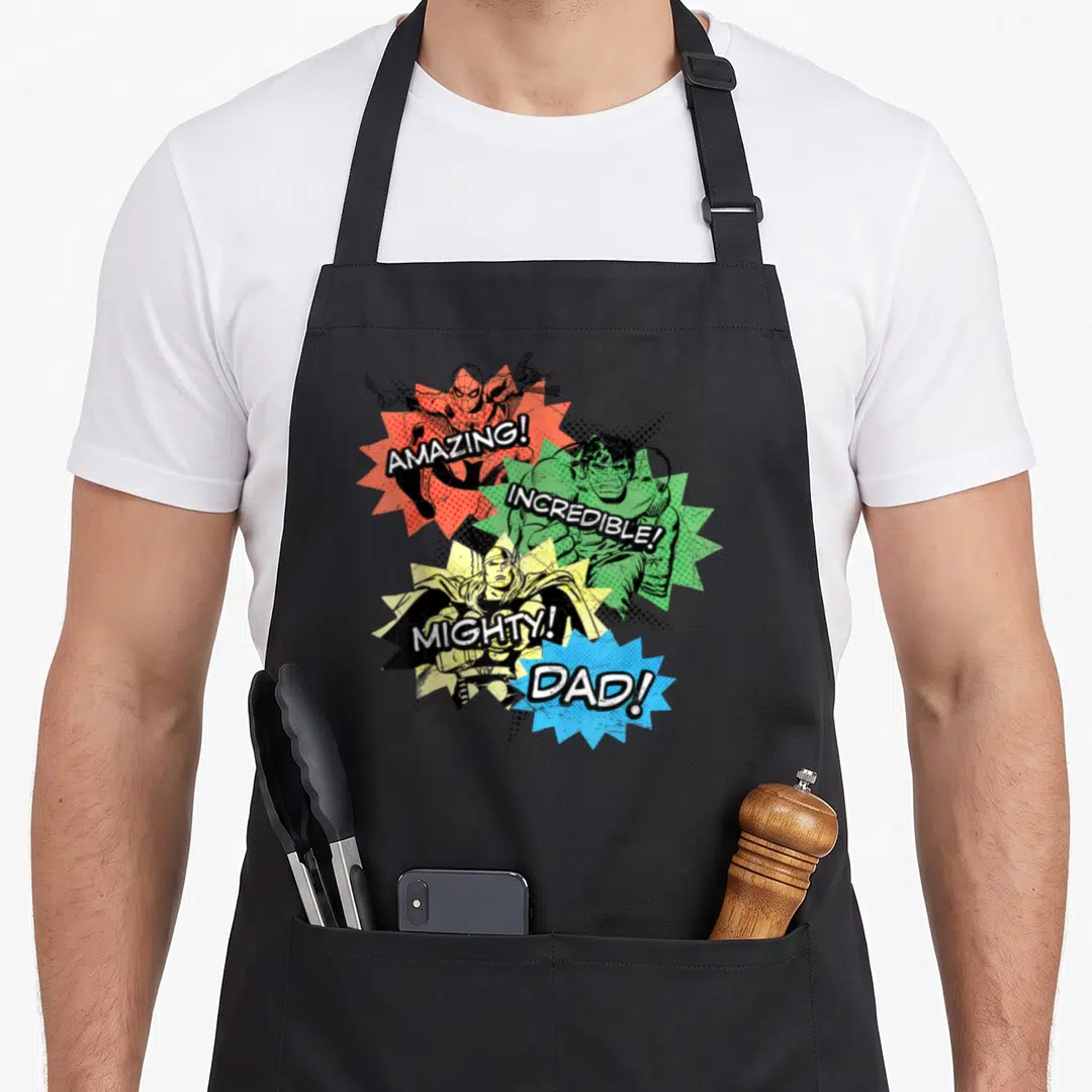 Amazing super hero aprons - Retro comic bursts with superheroes and text Amazing Incredible Mighty Dad in red green — shown on a black cotton canvas apron against a white background
