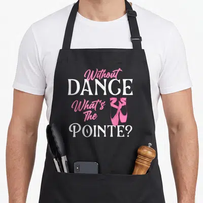 Dance pointe ballerina apron - Stacked text Without DANCE What's The POINTE beside pink pointe shoes — shown on a black cotton canvas apron against a white background