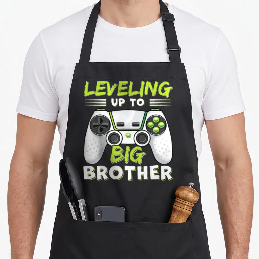 Leveling big brother apron - Game controller in white and lime green with LEVELING UP TO BIG BROTHER text in matching — shown on a black cotton canvas apron against a white background