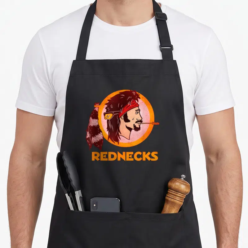 Washington football apron - Cartoon man head in orange circle with feather and REDNECKS text — shown on a black cotton canvas apron against a white background