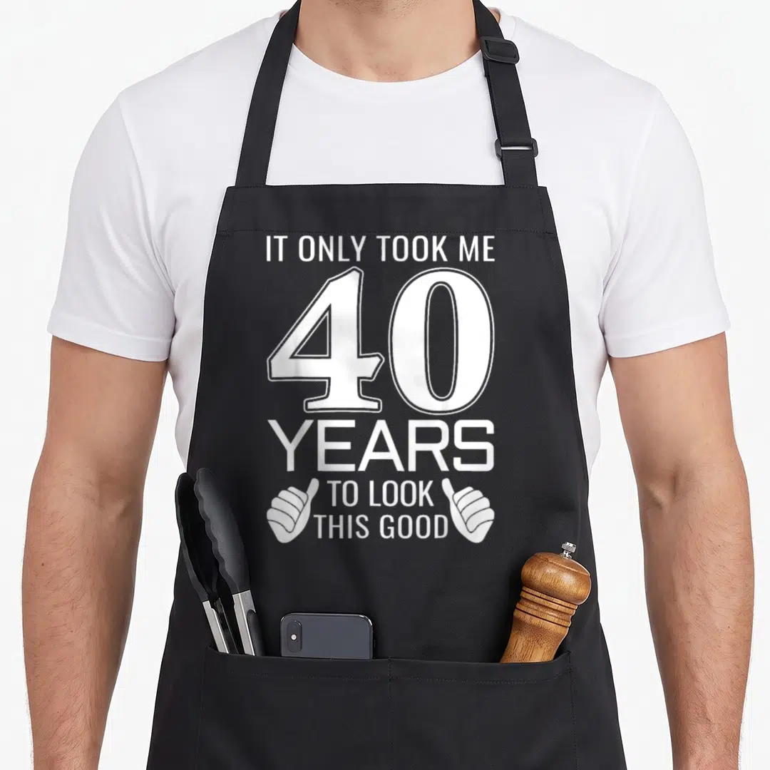 Took forties apron - White stacked text 40 YEARS TO LOOK THIS GOOD with two thumbs-up hands on either side of bottom — shown on a black cotton canvas apron against a white background
