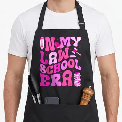 Era lawyer apron - Pink bubbly text reading IN MY LAW SCHOOL ERA with a pencil, gavel, and books scattered among small — shown on a black cotton canvas apron against a white background