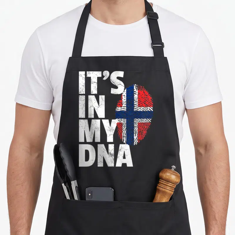 Dna norwegian kitchen aprons - Stacked white text IT'S IN MY DNA next to a red white and blue fingerprint flag — shown on a black cotton canvas apron against a white background