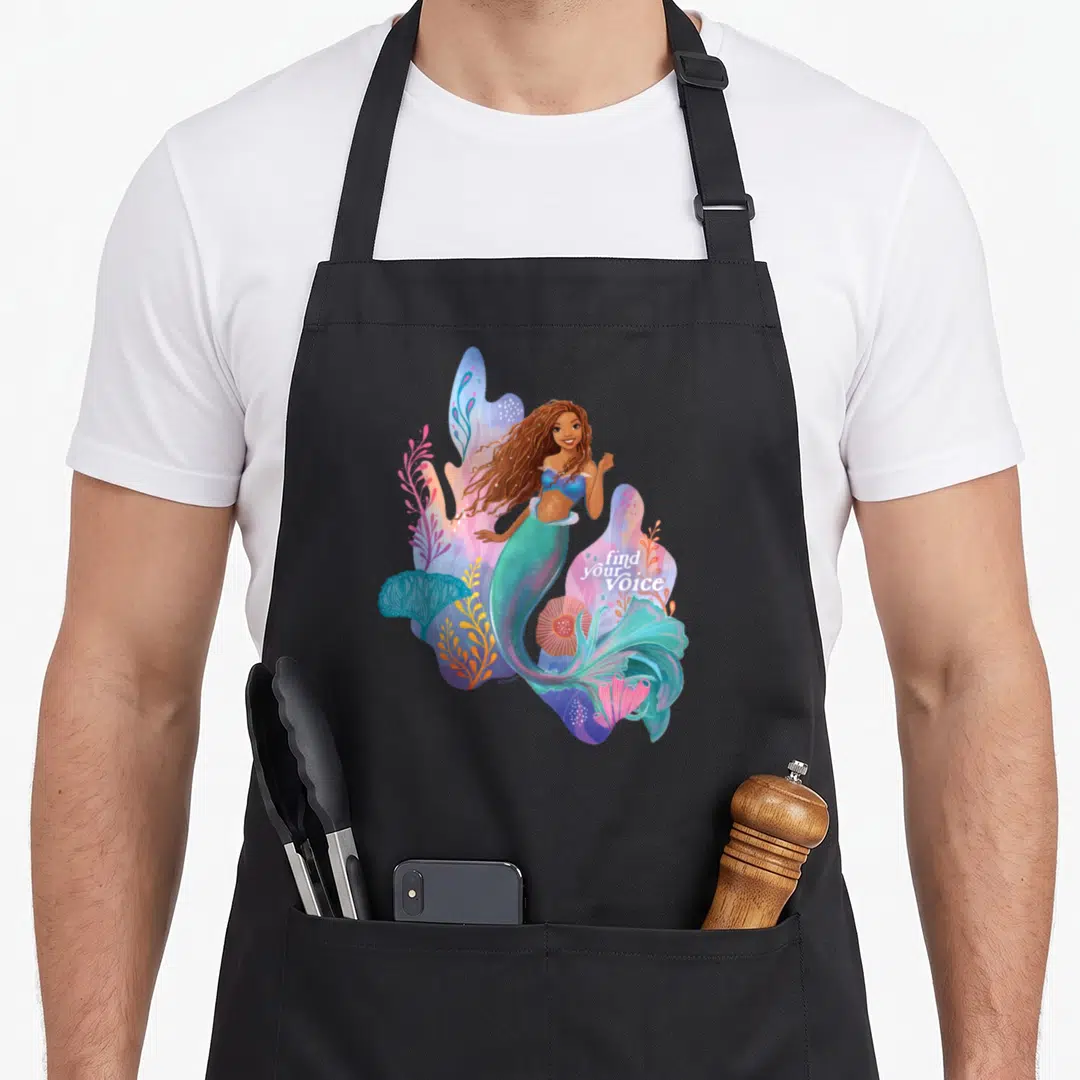 Find mermaid apron - Watercolor mermaid surrounded by teal pink blue and purple coral with find your Voice text — shown on a black cotton canvas apron against a white background