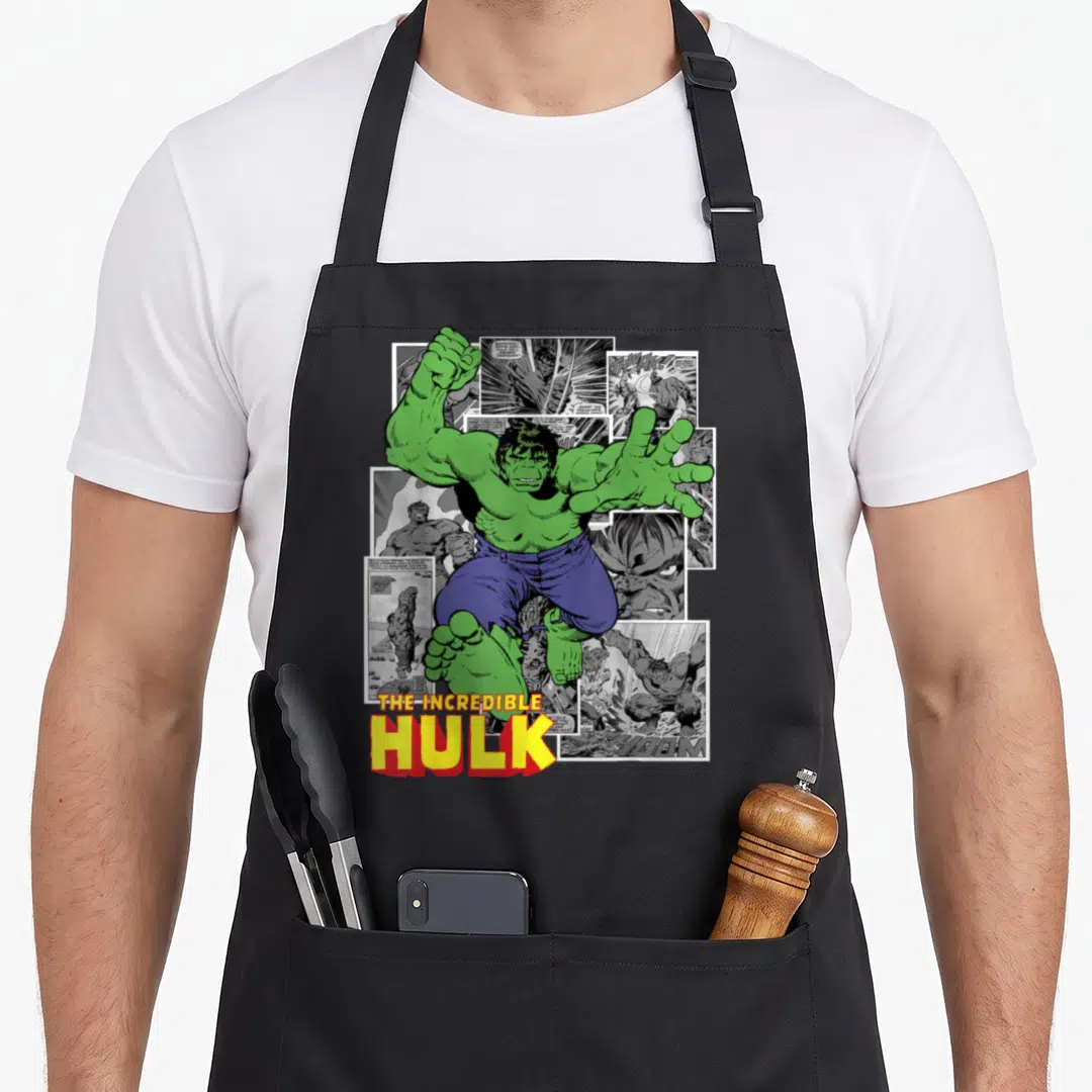 Panel hobby apron - Green Hulk figure leaping over black and white comic panels with yellow and red title text — shown on a black cotton canvas apron against a white background