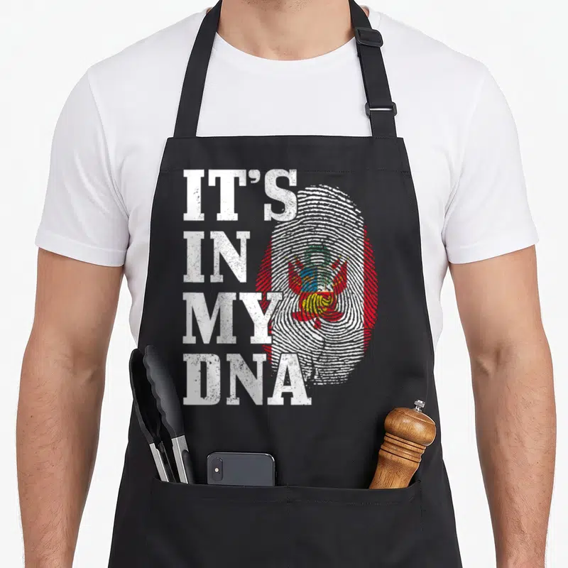 Dna peru apron - Stacked IT'S IN MY DNA text next to a distressed fingerprint containing a flag and coat of arms — shown on a black cotton canvas apron against a white background