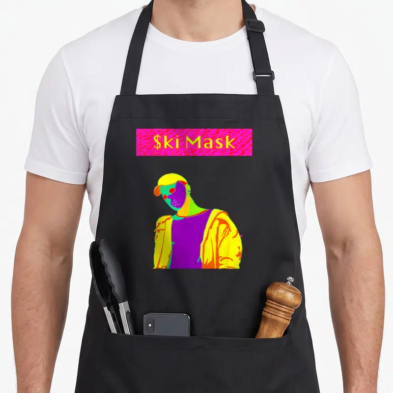 Mask slump apron - $kiMask text in pink rectangle above multi-colored cartoon person wearing a ski mask — shown on a black cotton canvas apron against a white background