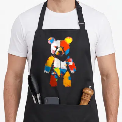 Motif bear apron - Multicolored teddy bear in red blue yellow and white cartoon style on black background — shown on a black cotton canvas apron against a white background