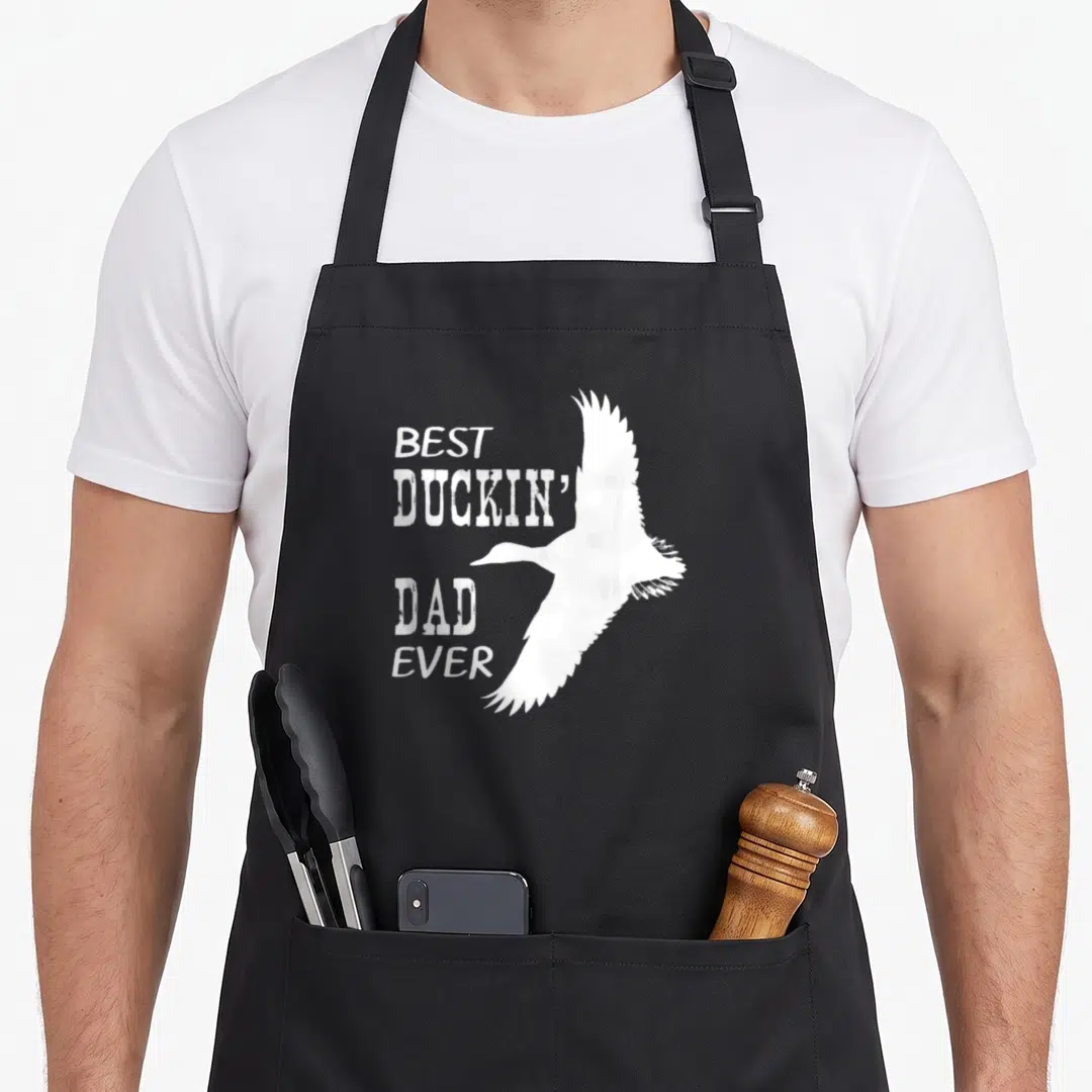 Duckin cotton duck apron - White distressed text Best Duckin' Dad Ever with flying duck silhouette — shown on a black cotton canvas apron against a white background