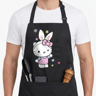 Talk easter apron - Hello Kitty in bunny ears with Talk to me I'm all ears text and flowers — shown on a black cotton canvas apron against a white background