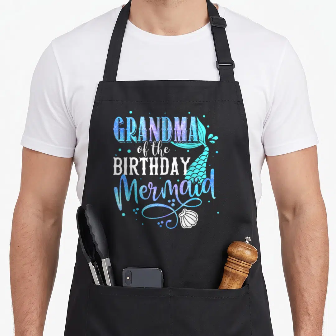 Birthday mermaid grandma in apron - Stacked text GRANDMA of the BIRTHDAY Mermaid with blue purple teal mermaid tail — shown on a black cotton canvas apron against a white background