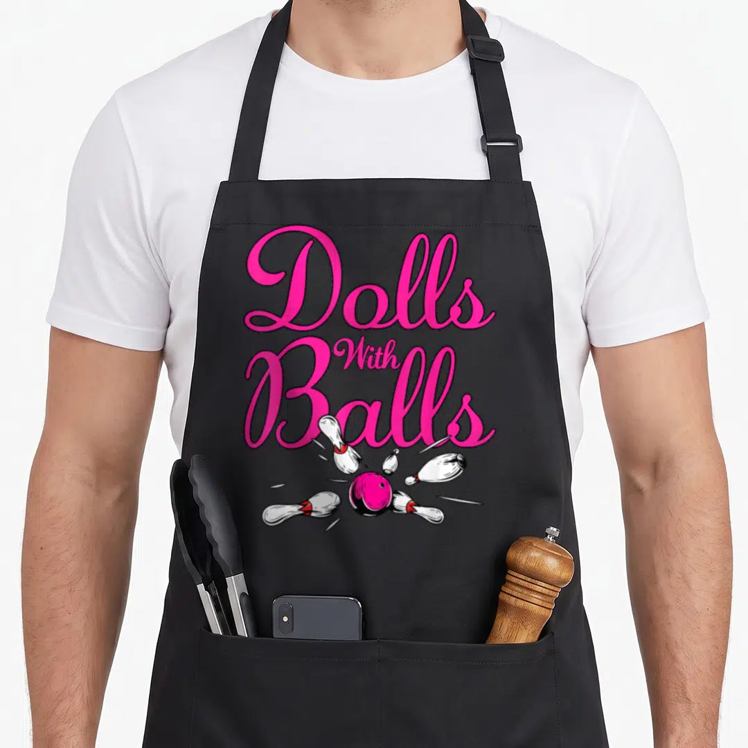 Ball doll apron - Pink script text reading Dolls With Balls above pink bowling ball scattering five white pins — shown on a black cotton canvas apron against a white background