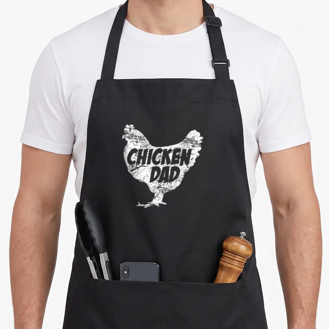 Father chicken apron - White distressed chicken silhouette containing the text CHICKEN DAD on a black background — shown on a black cotton canvas apron against a white background