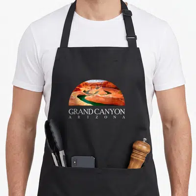 Arizona canyon apron - Semi-circle photo of canyon river with orange green blue rocks and text GRAND CANYON ARIZONA — shown on a black cotton canvas apron against a white background