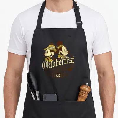 Friend oktoberfest apron - Mickey and Minnie in brown and gold Oktoberfest badge with pretzels and German text — shown on a black cotton canvas apron against a white background