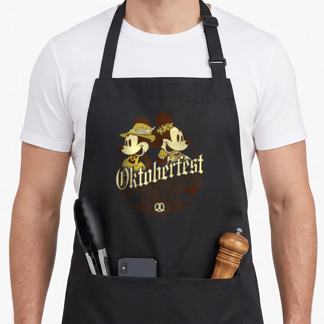 Friend oktoberfest apron - Mickey and Minnie in brown and gold Oktoberfest badge with pretzels and German text — shown on a black cotton canvas apron against a white background