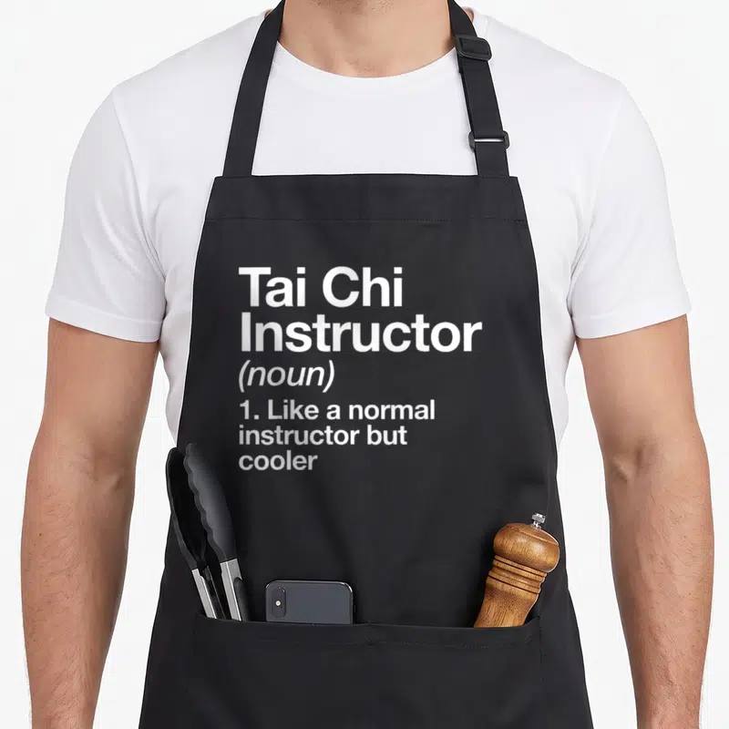 Tai chicha apron - White stacked text reading Tai Chi Instructor noun definition like normal but cooler — shown on a black cotton canvas apron against a white background