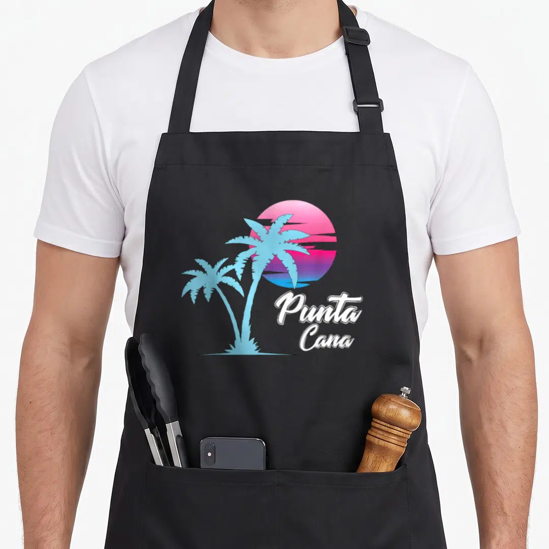 Dainty punta cana apron - Two blue palm trees on pink purple white gradient sun with Punta Cana text — shown on a black cotton canvas apron against a white background