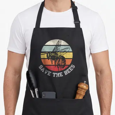 Distressed honey bee apron - Grey bee silhouette over five colored stripes with SAVE THE BEES text — shown on a black cotton canvas apron against a white background