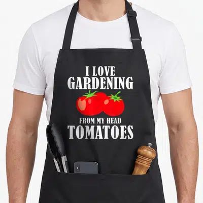 Vegetable gardener apron - I LOVE GARDENING FROM MY HEAD TOMATOES text with two red cartoon tomatoes — shown on a black cotton canvas apron against a white background