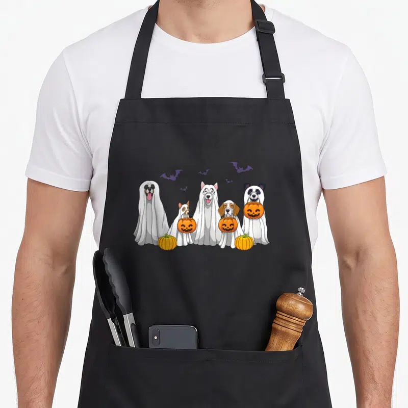 Dog halloween apron - Five white ghost dogs holding orange pumpkins with purple bats cartoon — shown on a black cotton canvas apron against a white background