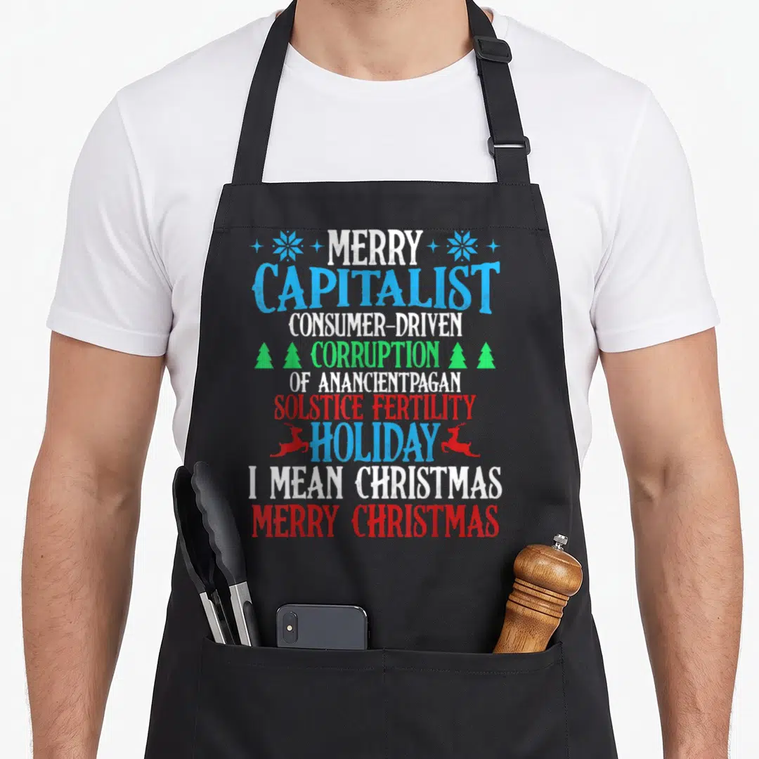 Capitalist retro christmas aprons - Stacked text reading Merry Capitalist Consumer-Driven Corruption of an Ancient — shown on a black cotton canvas apron against a white background