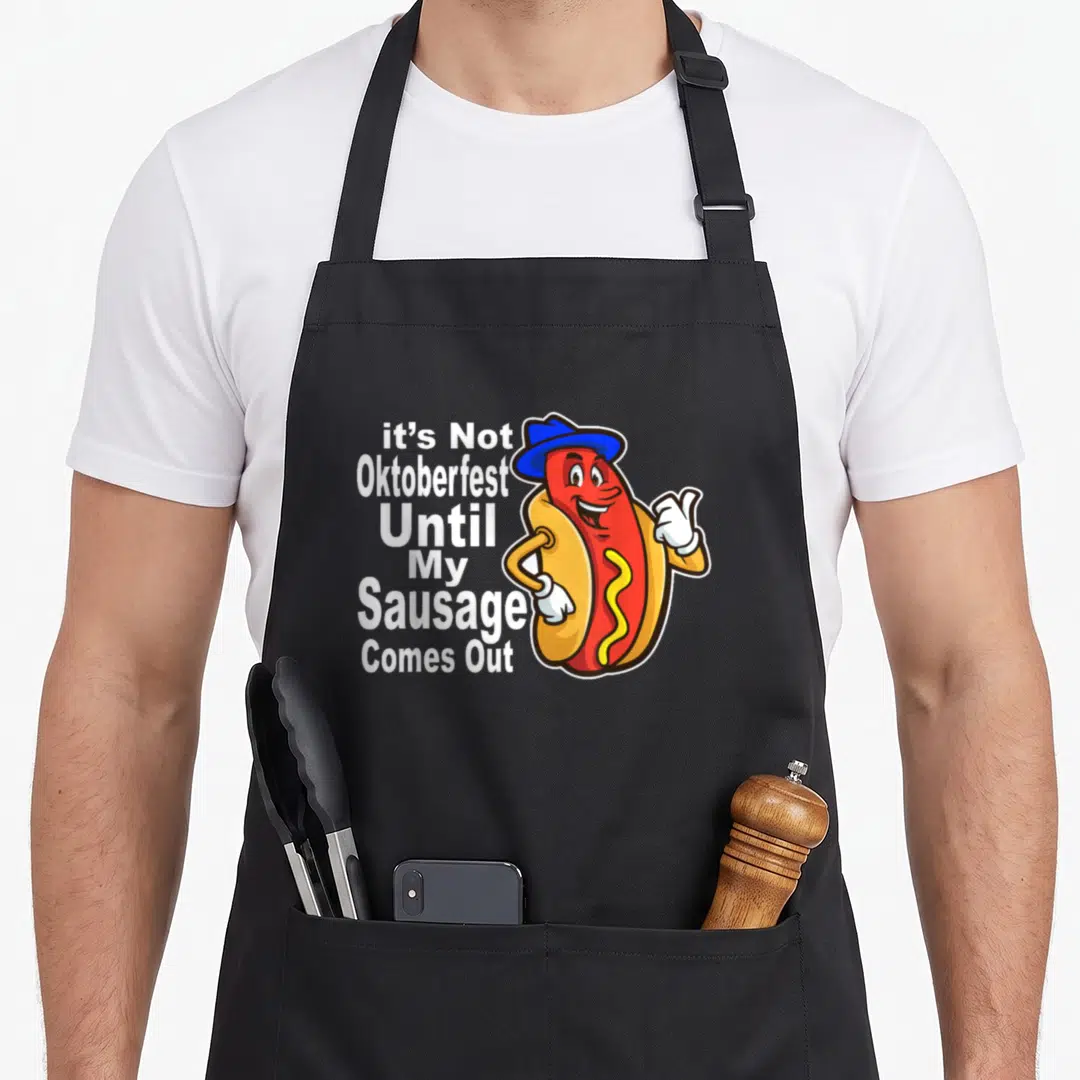 Meme sausage apron - Cartoon hot dog with blue hat next to stacked white text reading it's Not Oktoberfest Until My — shown on a black cotton canvas apron against a white background