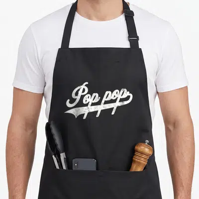 Pop papa apron - White distressed script text reading Pop pop with underline swoosh on grey background — shown on a black cotton canvas apron against a white background