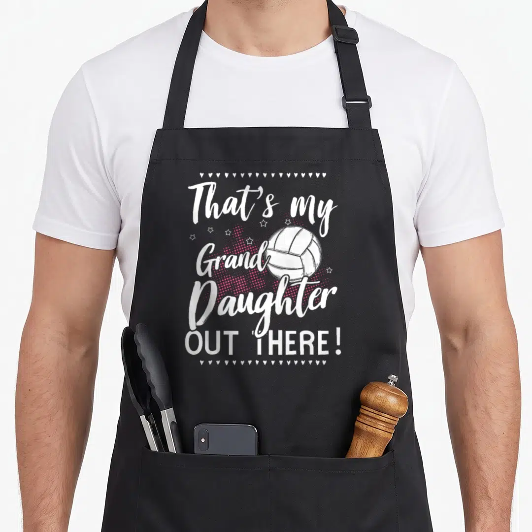 Player grandma granddaughter aprons - That's my Grand Daughter Out There text around volleyball with hearts and stars — shown on a black cotton canvas apron against a white background