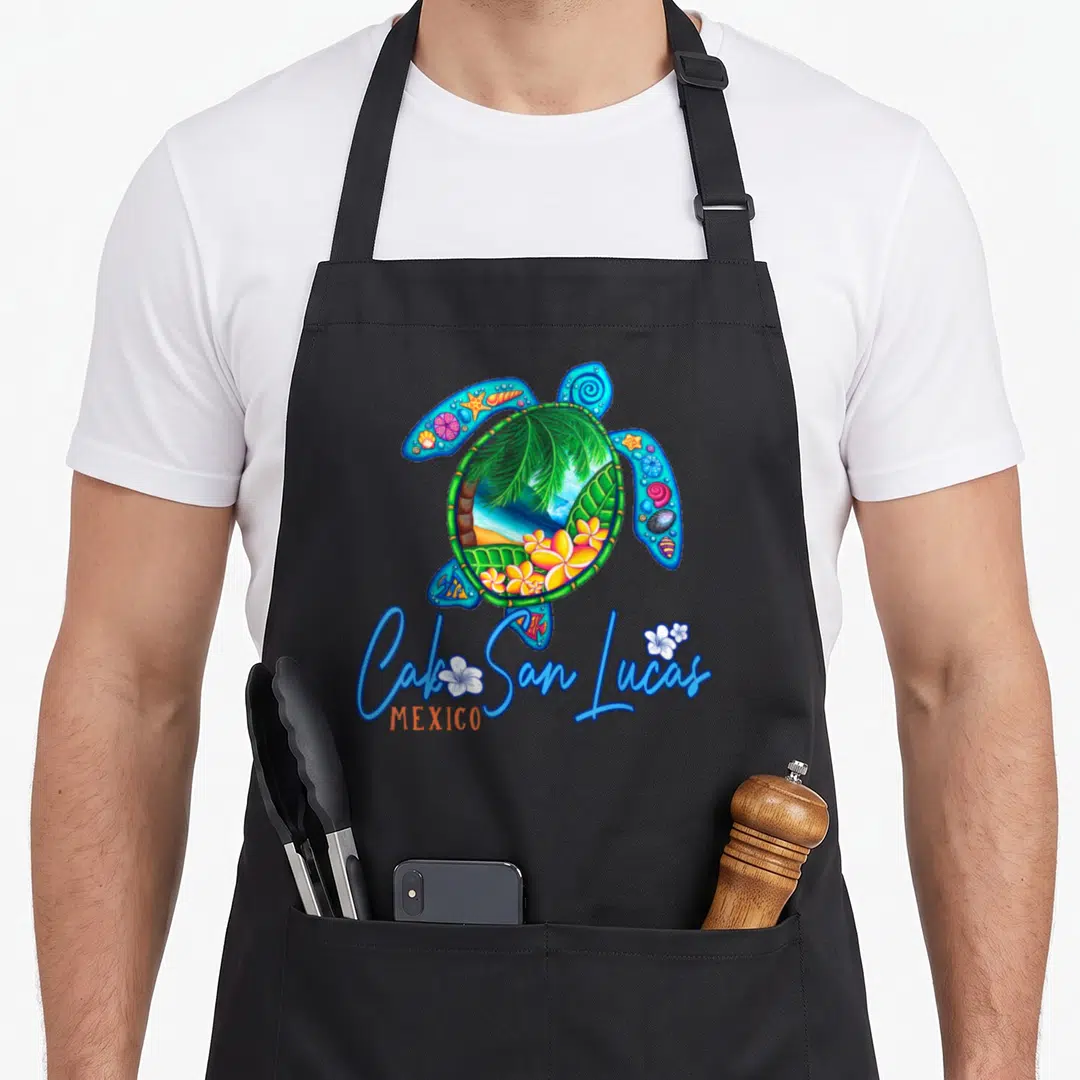 Lucas mexico apron - Cartoon sea turtle with tropical beach scene inside shell and blue Cabo San Lucas text — shown on a black cotton canvas apron against a white background