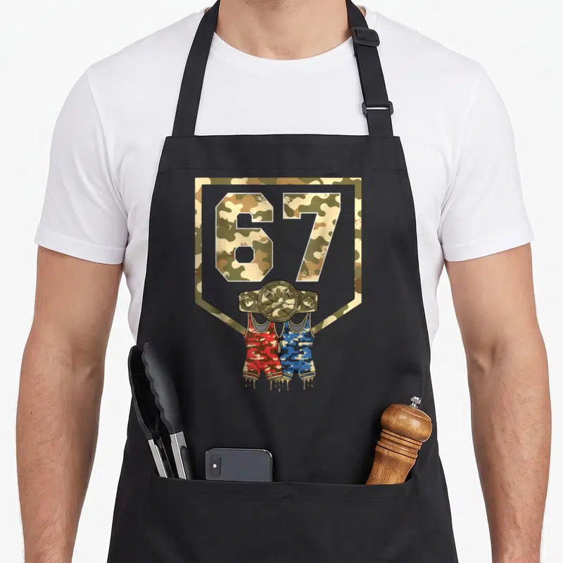 Wrestling camo apron - Number 67 camo shield with belt and red blue shorts hanging below — shown on a black cotton canvas apron against a white background