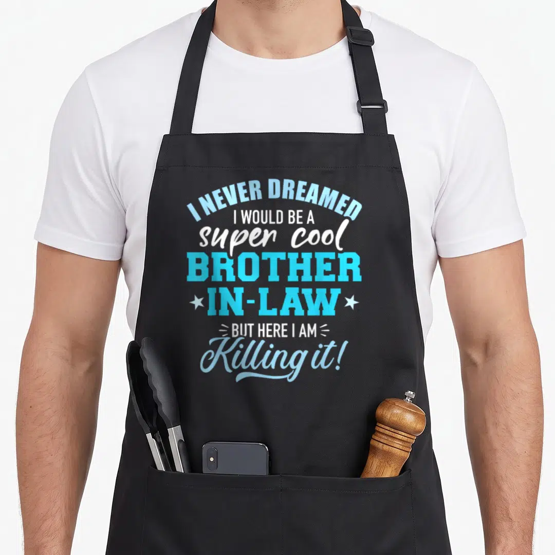 Dreamed law humor apron - Stacked blue and white typography saying I Never Dreamed I Would Be A Super Cool Brother — shown on a black cotton canvas apron against a white background