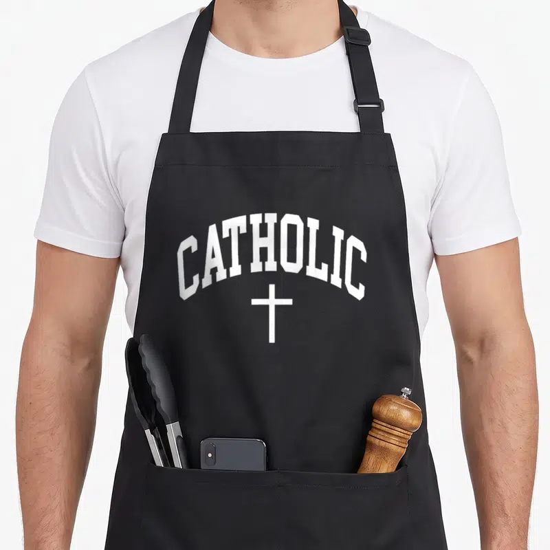 Believe catholic apron - White arched CATHOLIC text above a small cross symbol on grey background — shown on a black cotton canvas apron against a white background