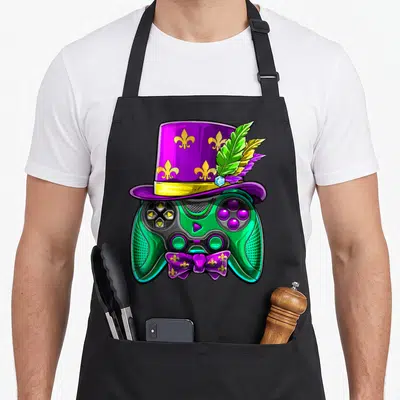 Video mardi gras aprons - Green game controller wearing purple top hat with yellow fleur-de-lis and matching bow tie — shown on a black cotton canvas apron against a white background