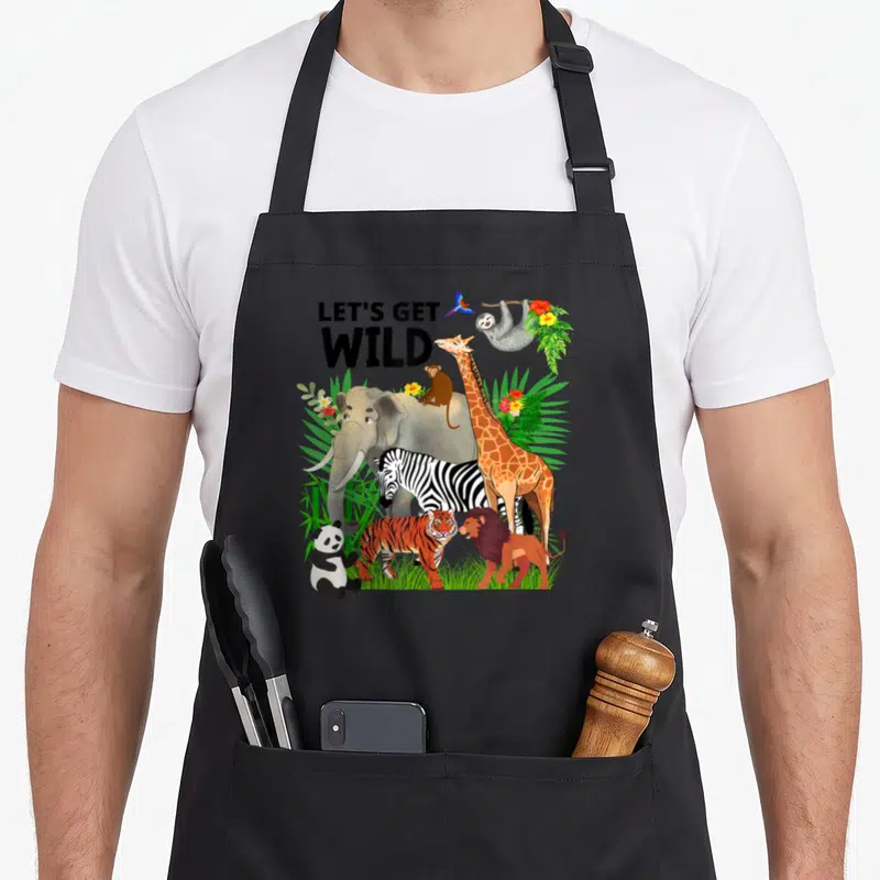 Wildlife safari birthday apron - Cartoon elephant giraffe zebra and lion under LETS GET WILD text surrounded — shown on a black cotton canvas apron against a white background
