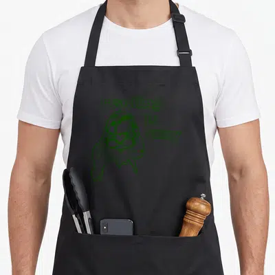 Rory bookworm apron - green line art woman with glasses and stacked text reading issexy — shown on a black cotton canvas apron against a white background